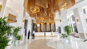 Un amplio vestíbulo con un mostrador de recepción central, plantas en macetas grandes y un moderno candelabro.