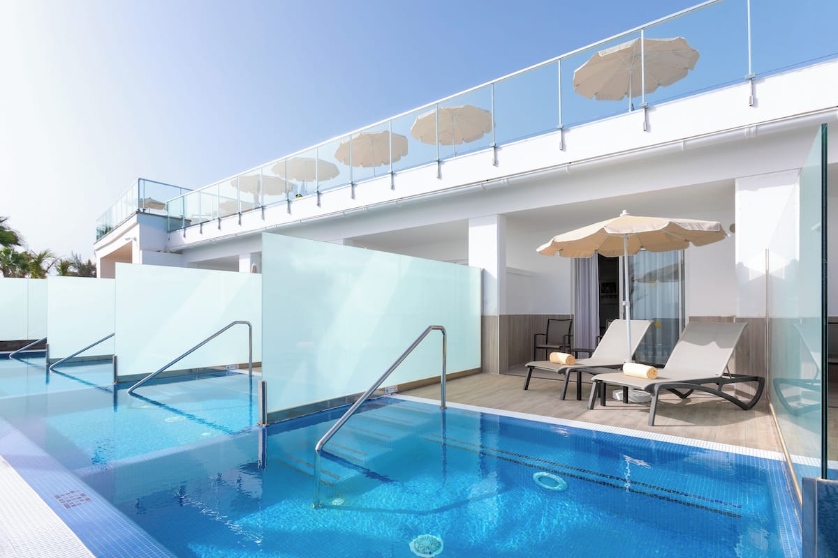 A swimming pool with glass railings, lounge chairs, and umbrellas.