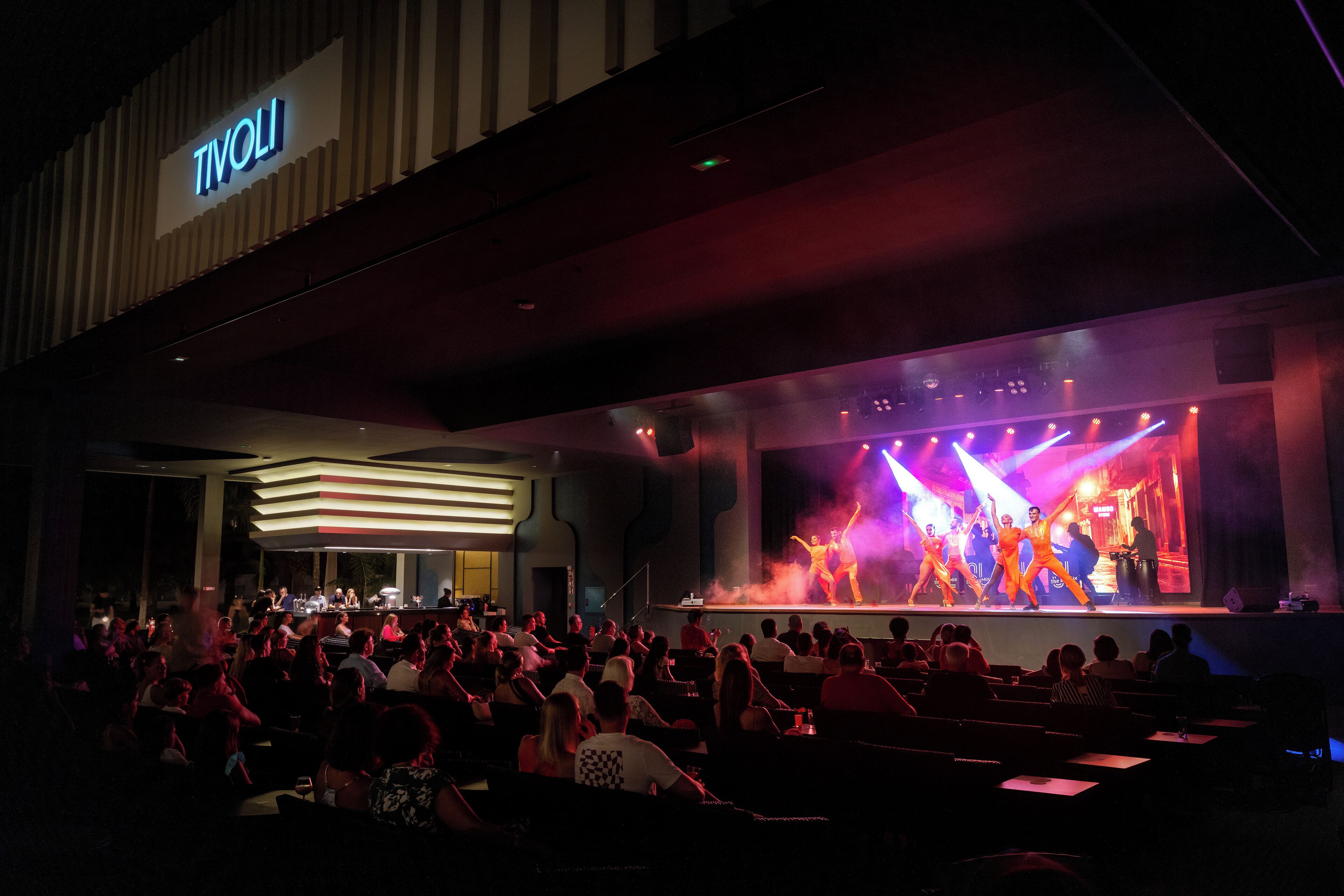 A theater with a stage performance, seating area, and a sign that reads "TIVOLI".