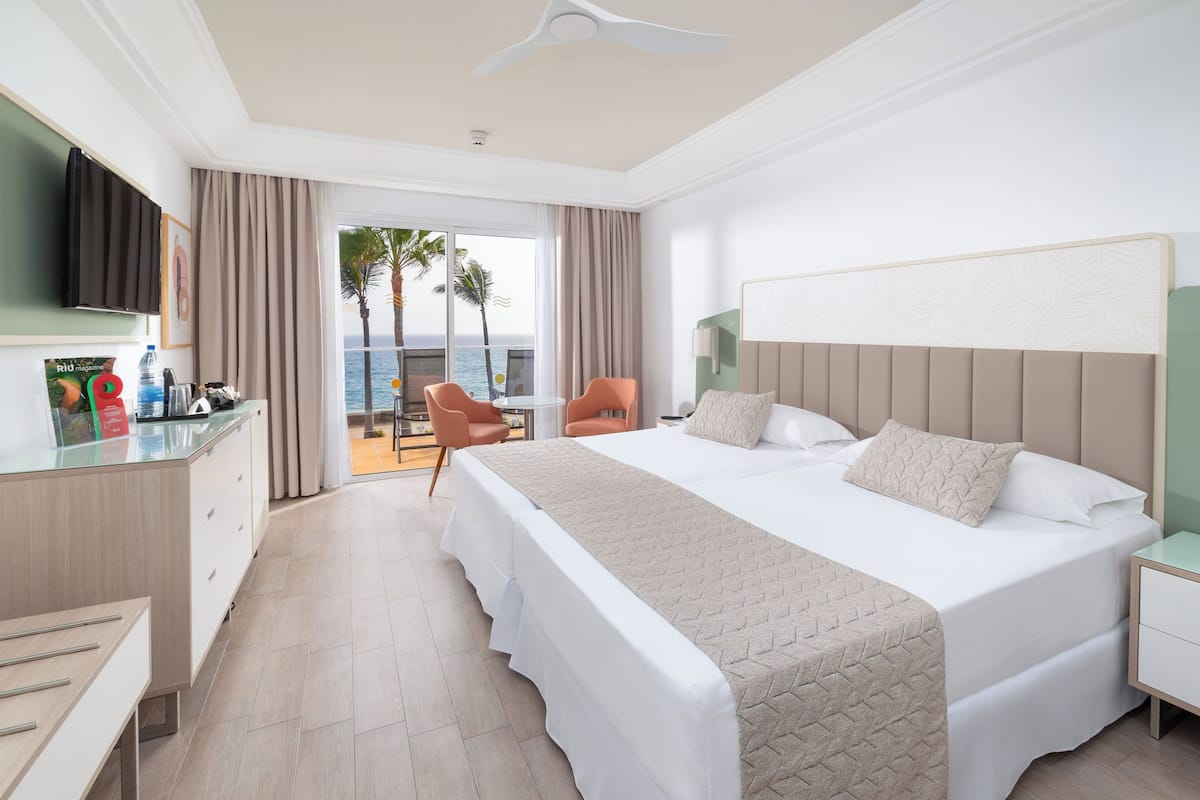 A hotel room with a large bed, a desk, a chair, and a view of the ocean.