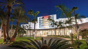 Un hôtel moderne, reconnaissable à son grand panneau « RIU », entouré de palmiers et agrémenté d’un aménagement paysager soigné.