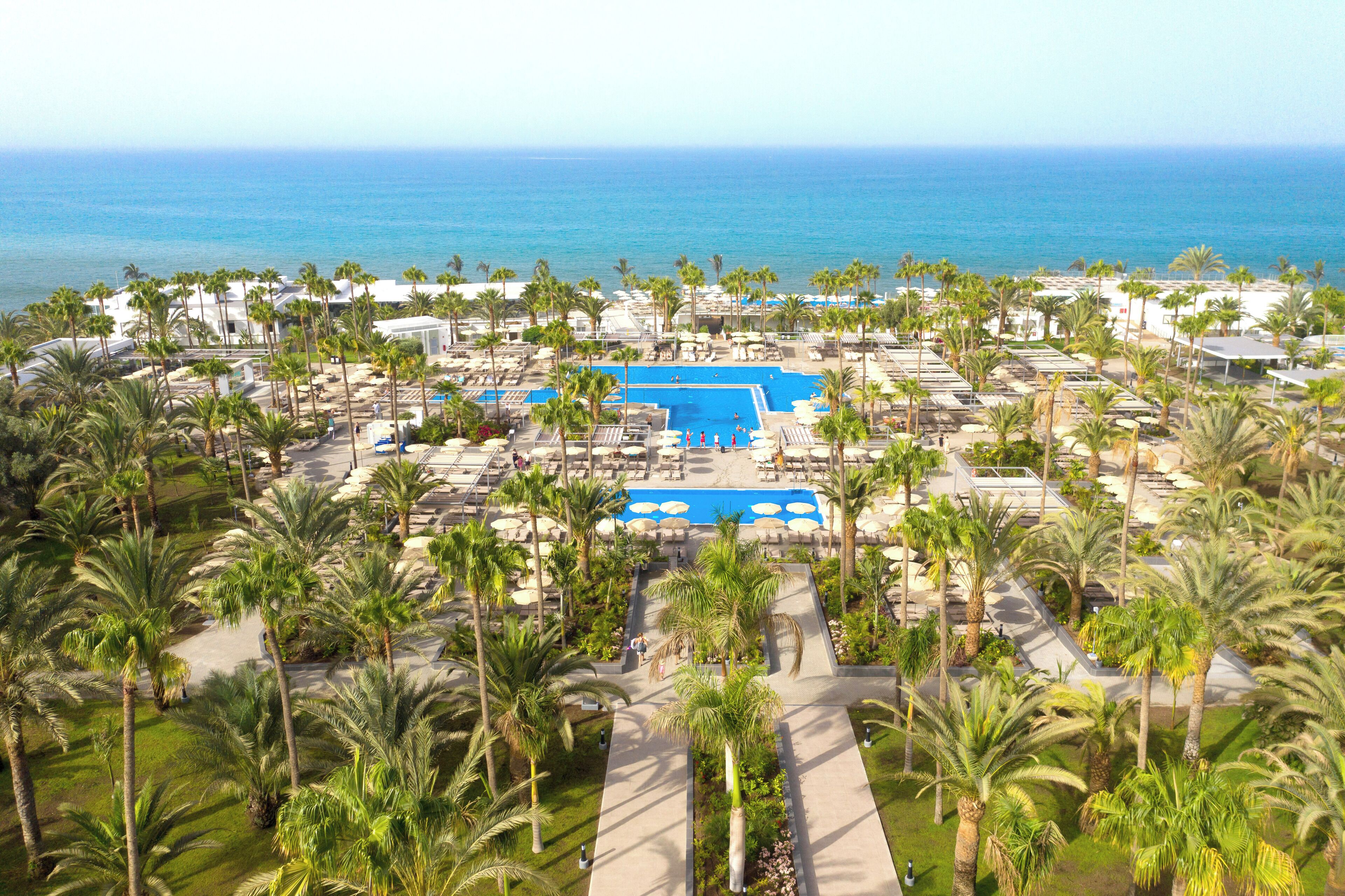 Een resort met meerdere zwembaden, palmbomen en uitzicht op de oceaan.