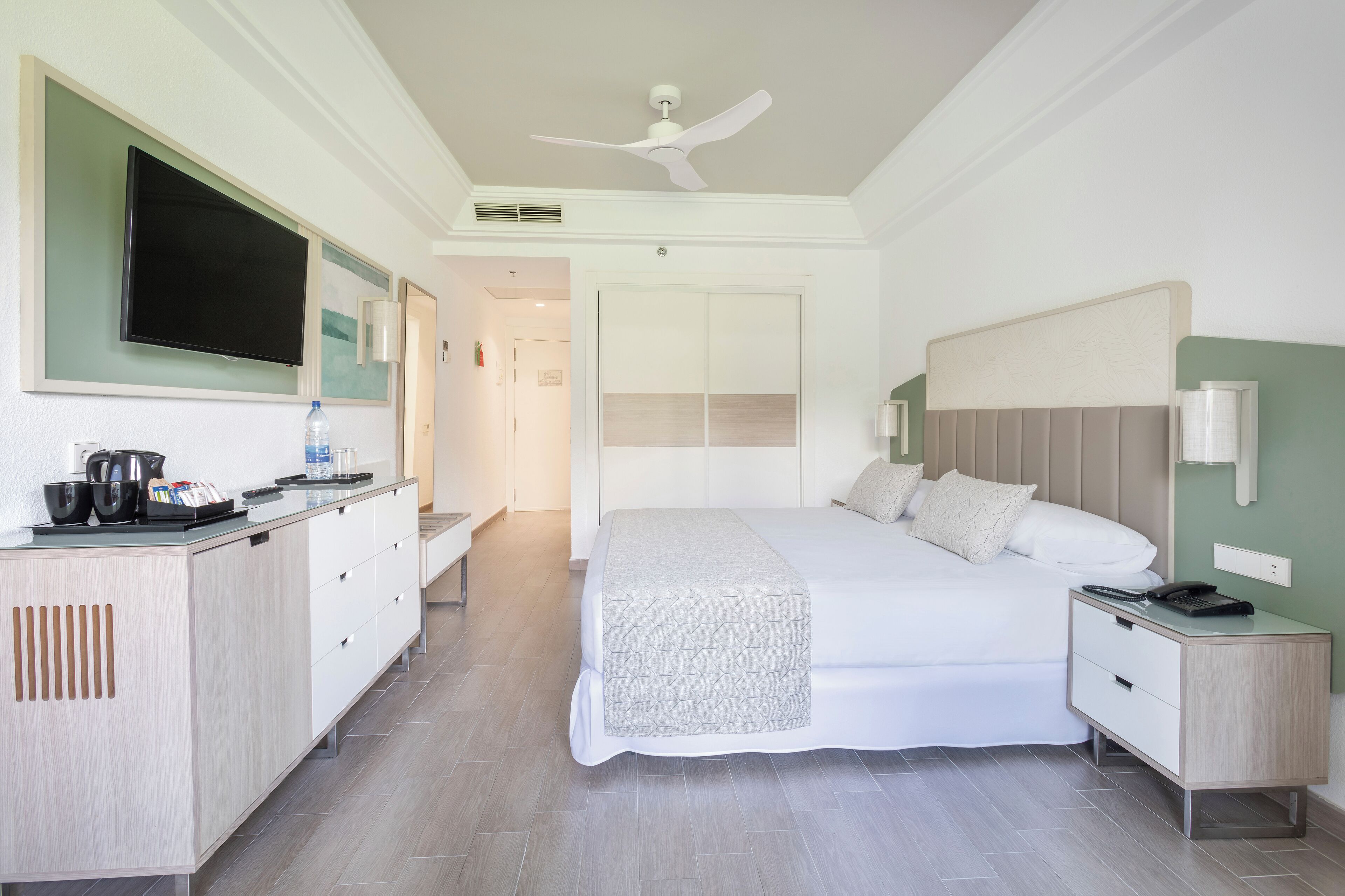Una habitación de hotel moderna con una cama grande, mesita de noche y un televisor de pantalla plana montado en la pared.
