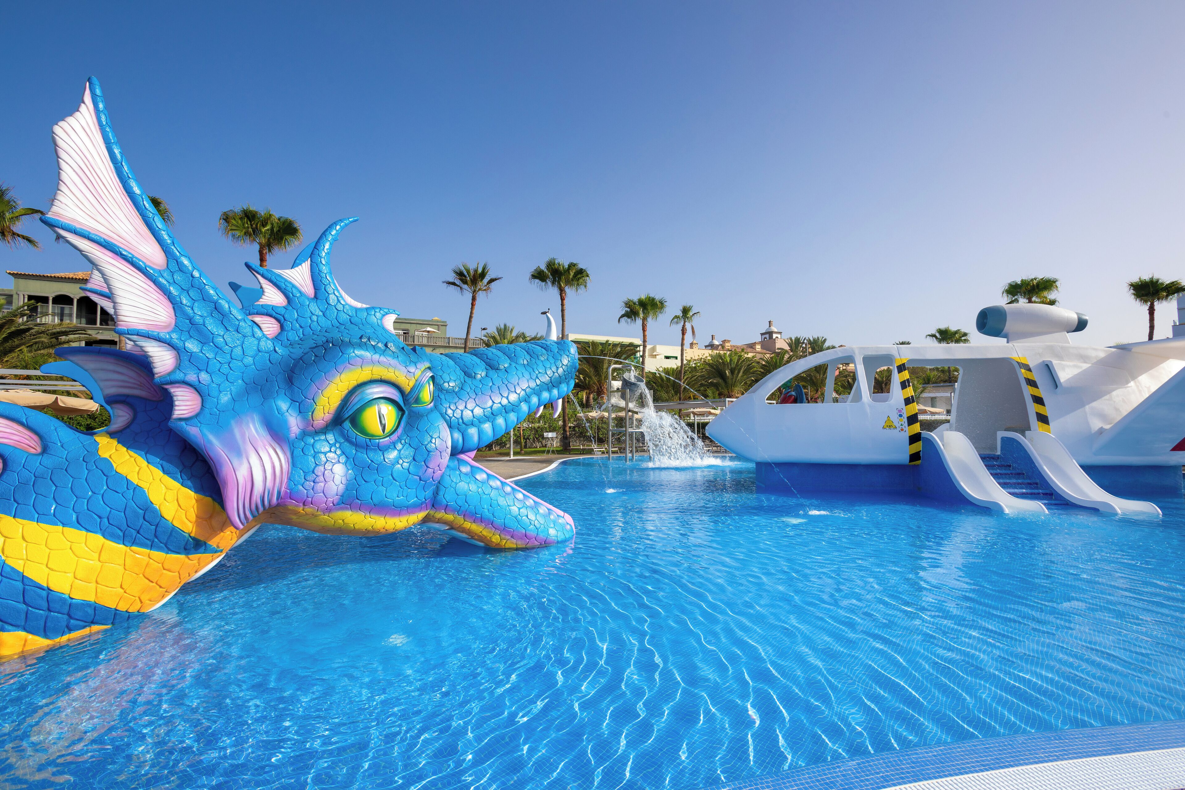 Una piscina con una decoración de dragón, un tobogán y palmeras al fondo.