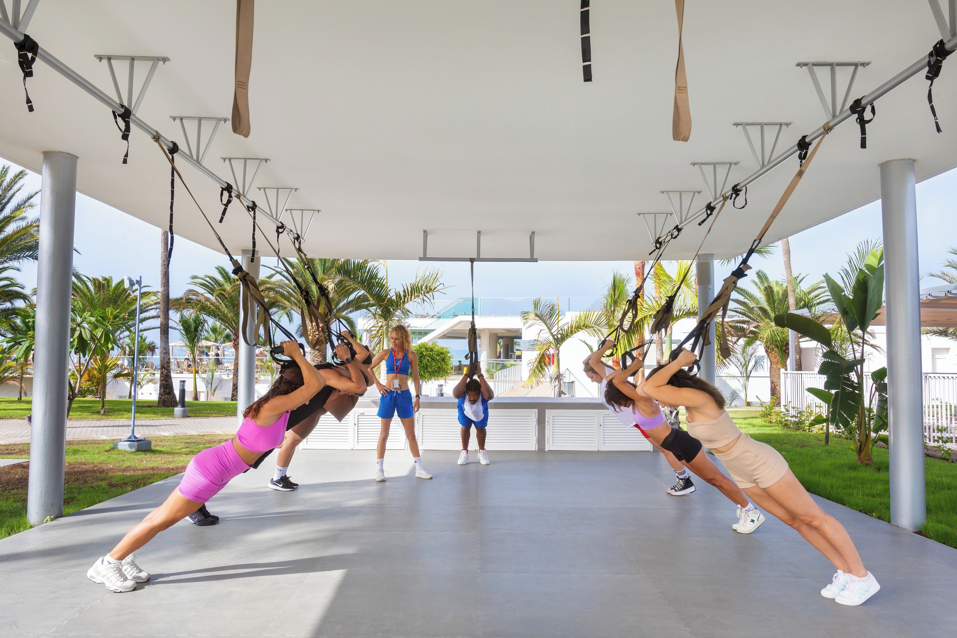 A group of people performing a workout under a covered area with exercise equipment.