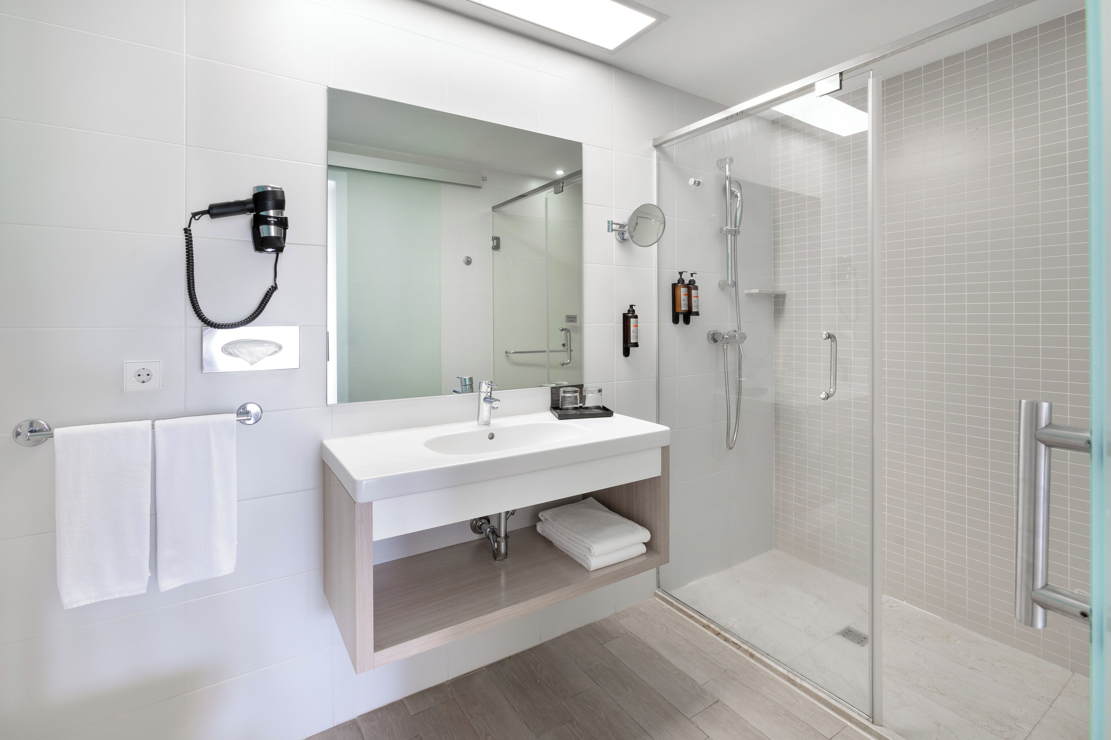 Un baño moderno con cabina de ducha de vidrio, un lavabo blanco y un espejo grande.
