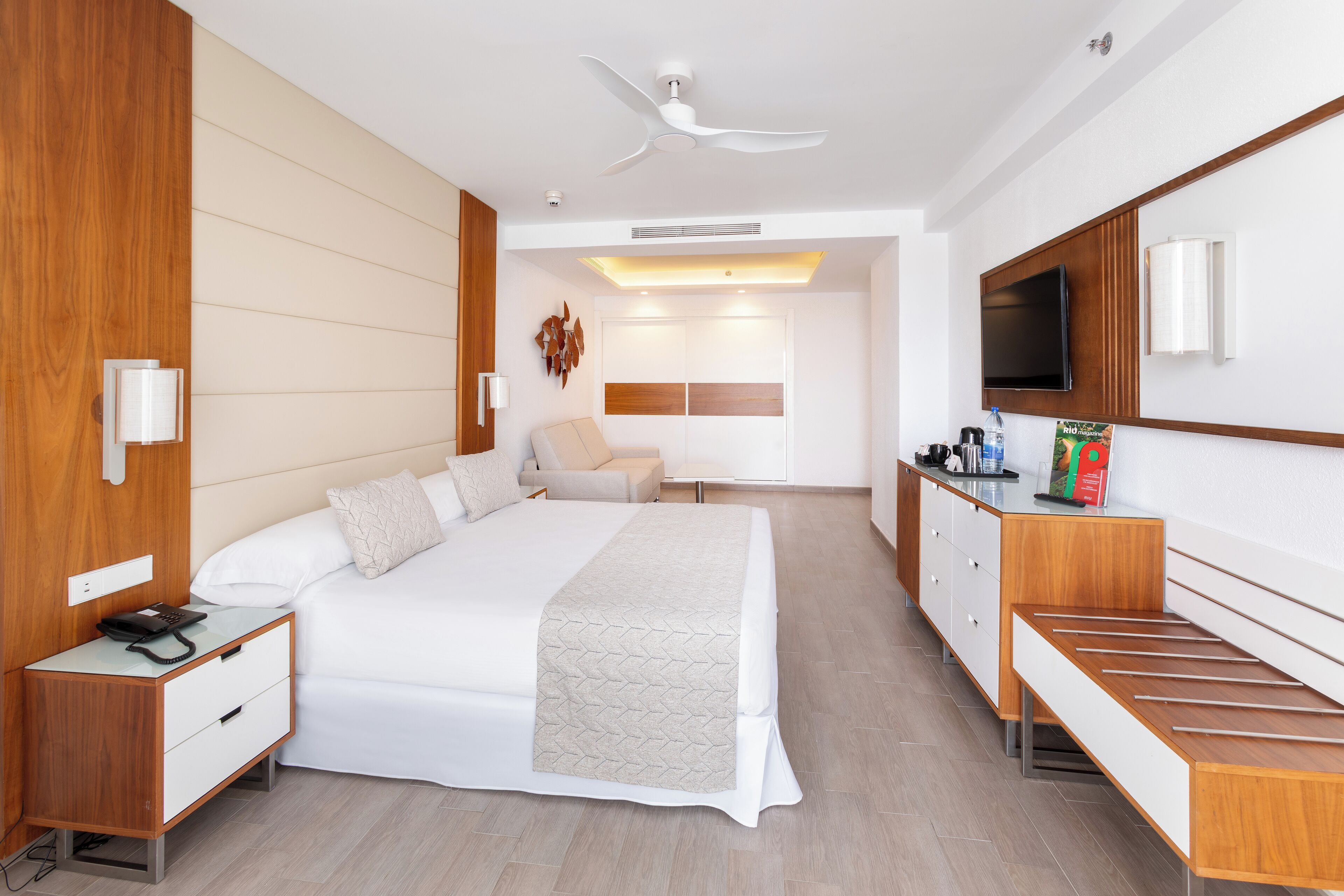 Una habitación de hotel moderna con una cama grande, un escritorio, un televisor de pantalla plana y un ventilador de techo.