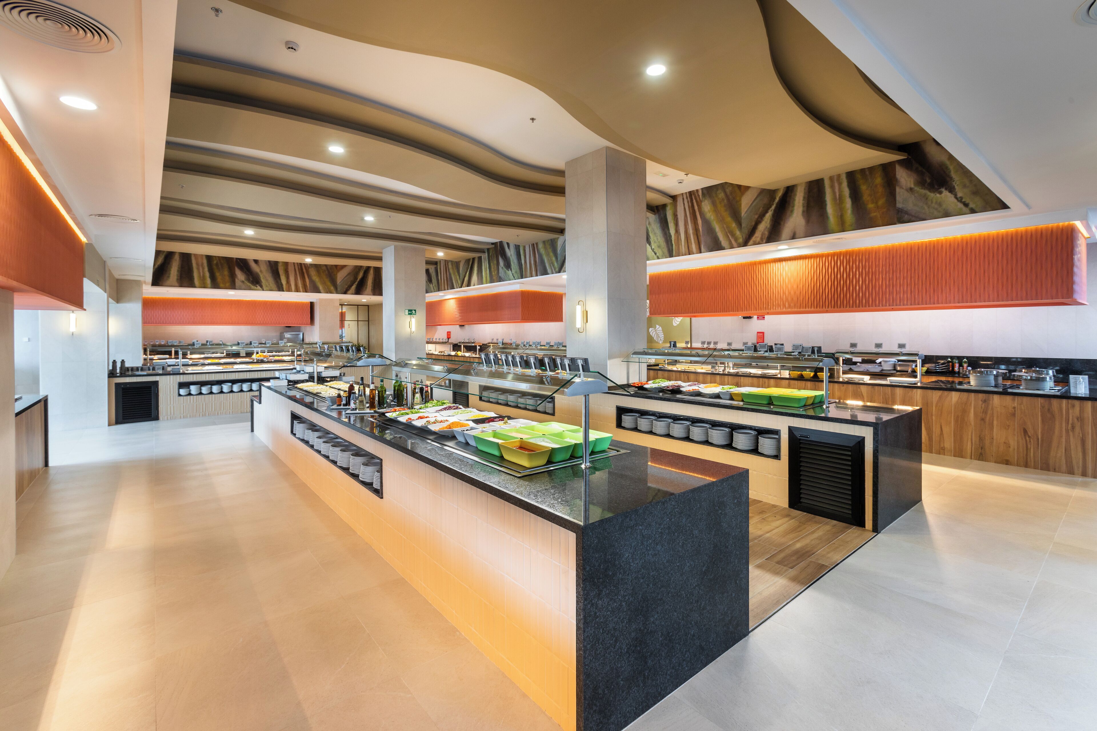 Un área de buffet moderna con múltiples estaciones de comida, un mostrador de servicio central y un diseño limpio y contemporáneo.