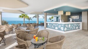 Un espace bar situé au bord de la plage, avec des meubles en osier et une vue sur l’océan.