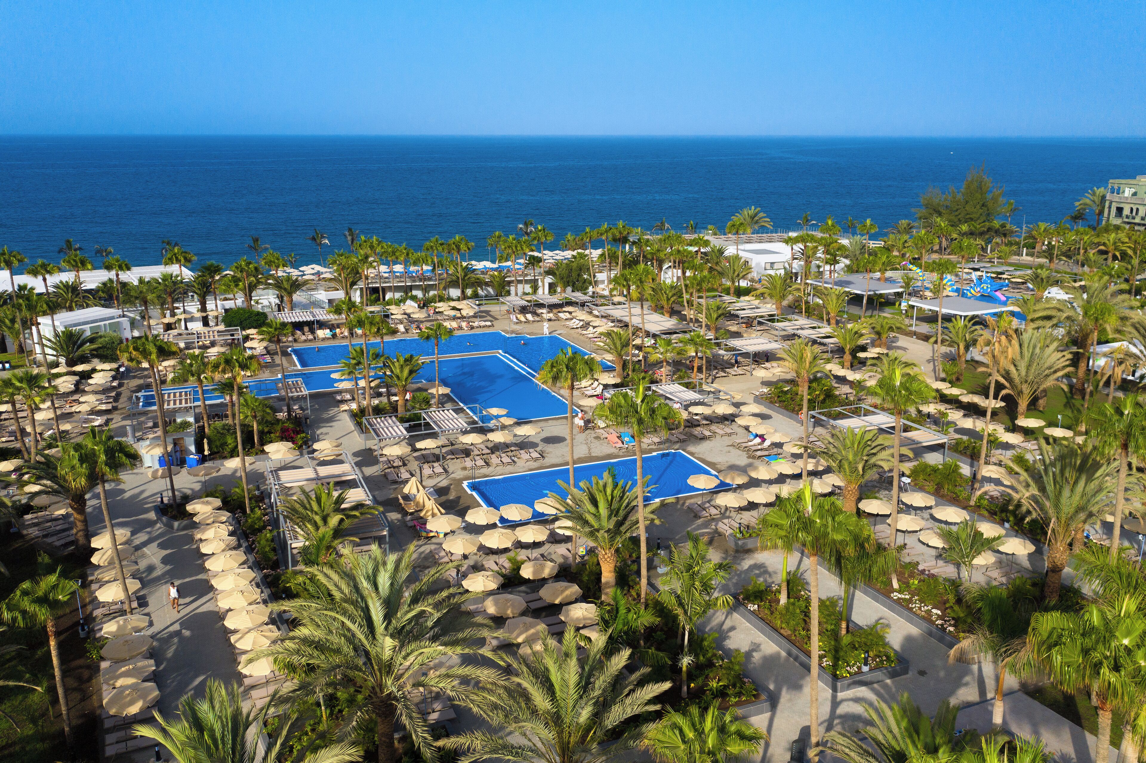 Un resort con varias piscinas, palmeras y vista al océano.