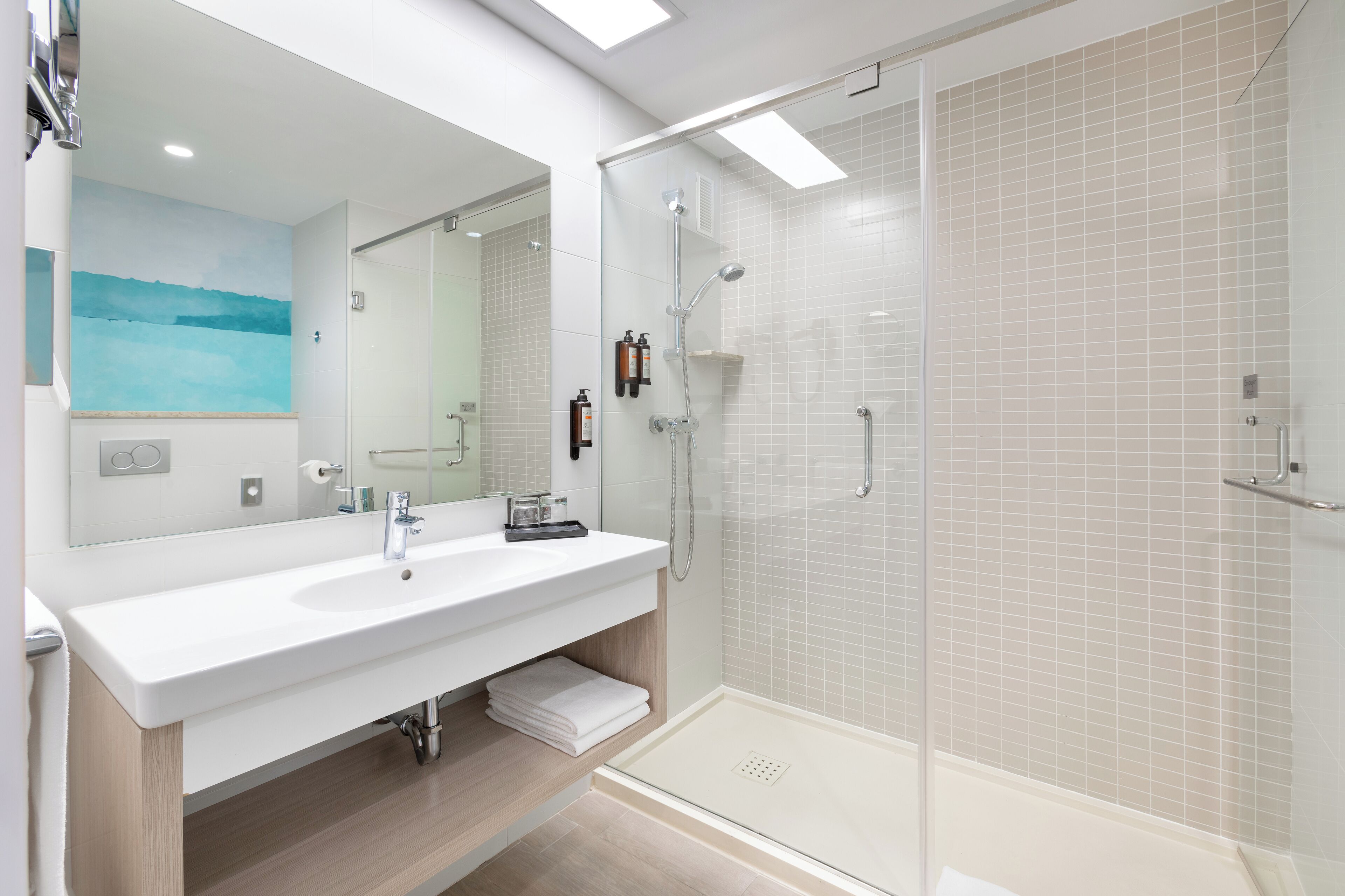 Un baño moderno con un espejo grande, lavabo blanco y cabina de ducha con paredes de vidrio.