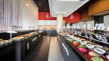 A buffet with various food items and a seating area in the background.