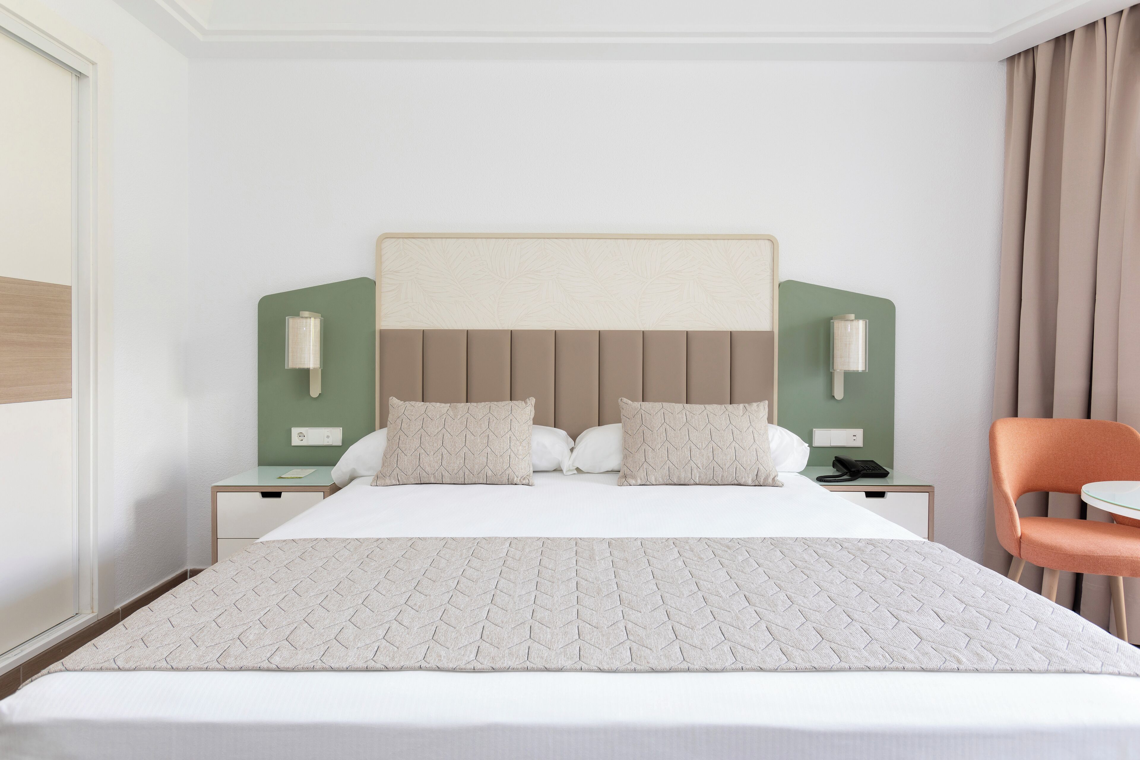 Habitación de hotel con una cama grande, dos mesitas de noche, una silla y una pared decorada en verde.