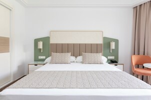 A hotel room with a large bed, two bedside tables, a chair, and a green accent wall.
