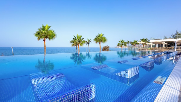 Une piscine à débordement à l’eau d’un bleu cristallin, bordée de palmiers et offrant une vue sur l’océan.