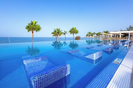 An infinity pool with clear blue water, palm trees, and a view of the ocean.
