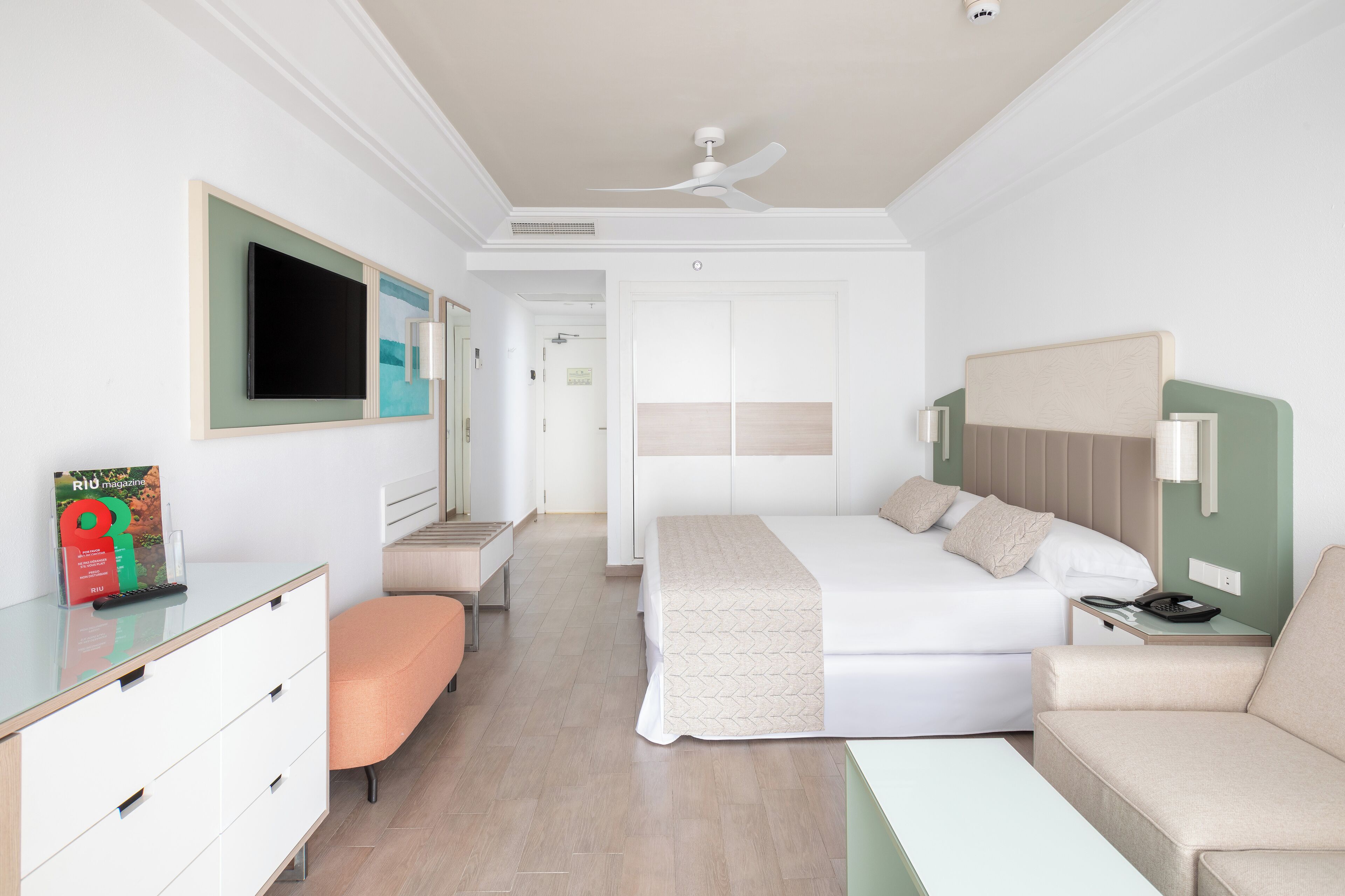 A hotel room with a bed, a desk, a chair, a television, and a ceiling fan.