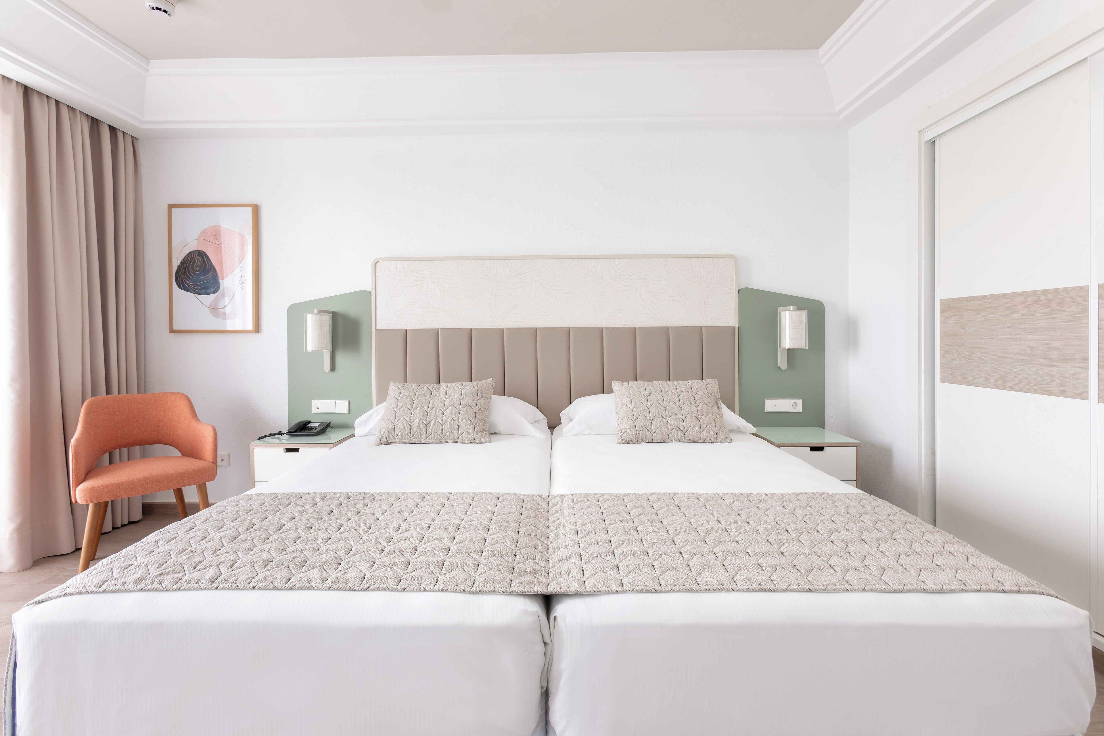 Habitación de hotel con una cama grande, dos mesitas de noche, una silla y un cuadro en la pared.