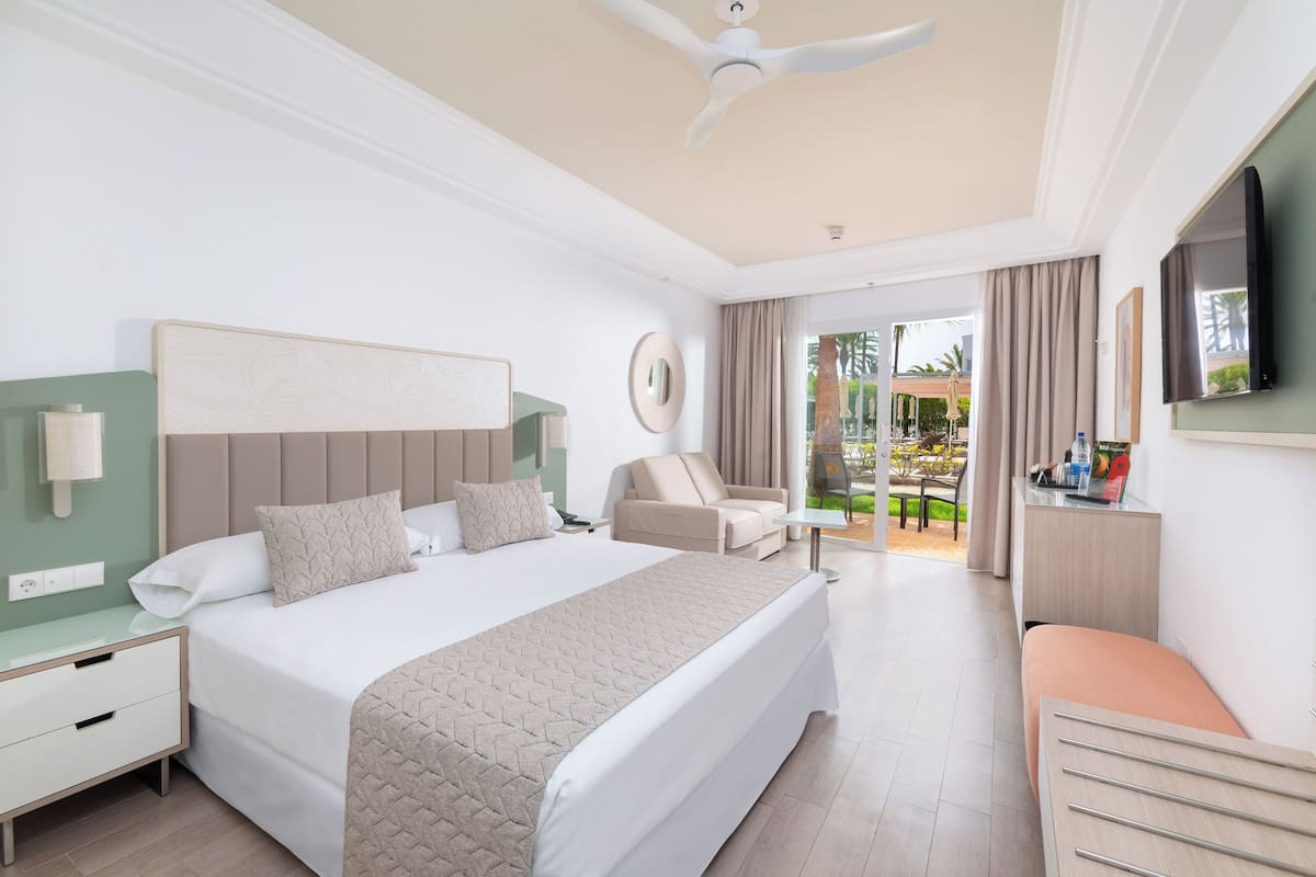 A modern hotel room with a large bed, a desk, a chair, and a TV.