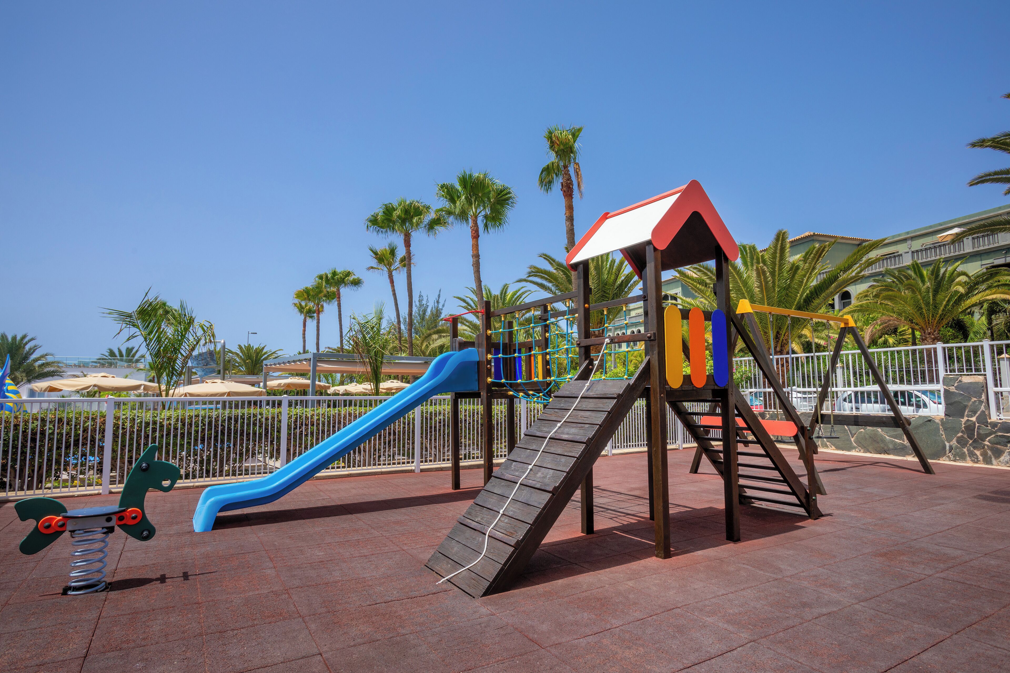 A playground with a blue slide, a wooden climbing structure, and a horse-shaped swing set.