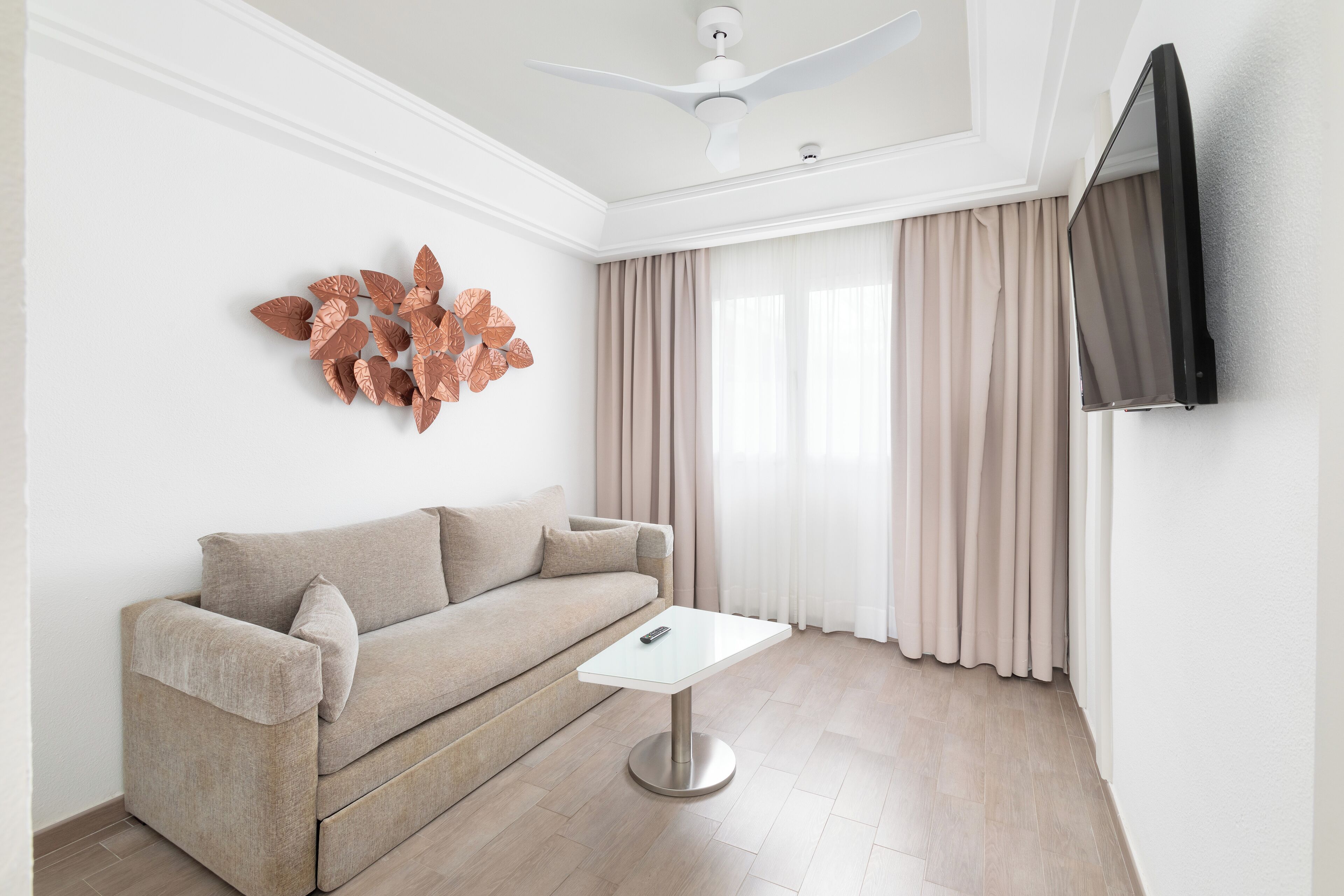 Una sala de estar moderna con un sofá, una mesa de centro, un ventilador de techo, un televisor montado en la pared y un elemento decorativo en la pared.