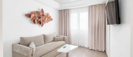 Una sala de estar moderna con un sofá, una mesa de centro, un ventilador de techo, un televisor montado en la pared y un elemento decorativo en la pared.