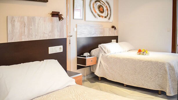 A hotel room with two beds, a nightstand, a desk, and a wall-mounted lamp.