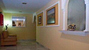 A hallway with a beige wall, a window with a decorative shelf, and a framed picture.