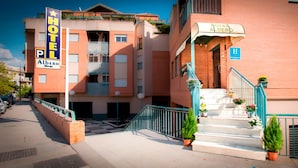 A hotel named "Hotel Albero" with a signboard, a staircase with potted plants, and a blue railing.