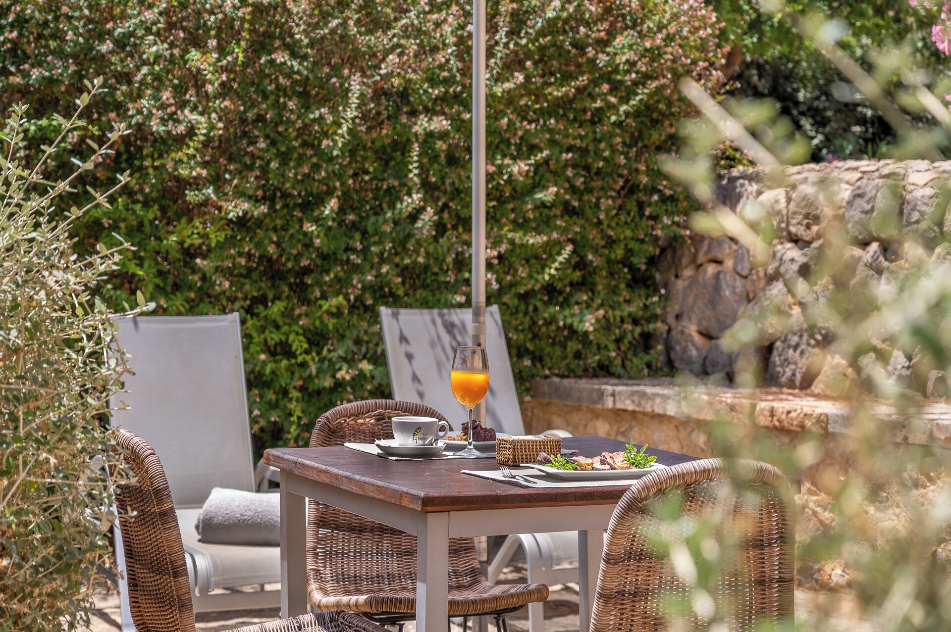 An outdoor dining area with wicker furniture, a table with a glass of orange juice, and a stone wall in the background.