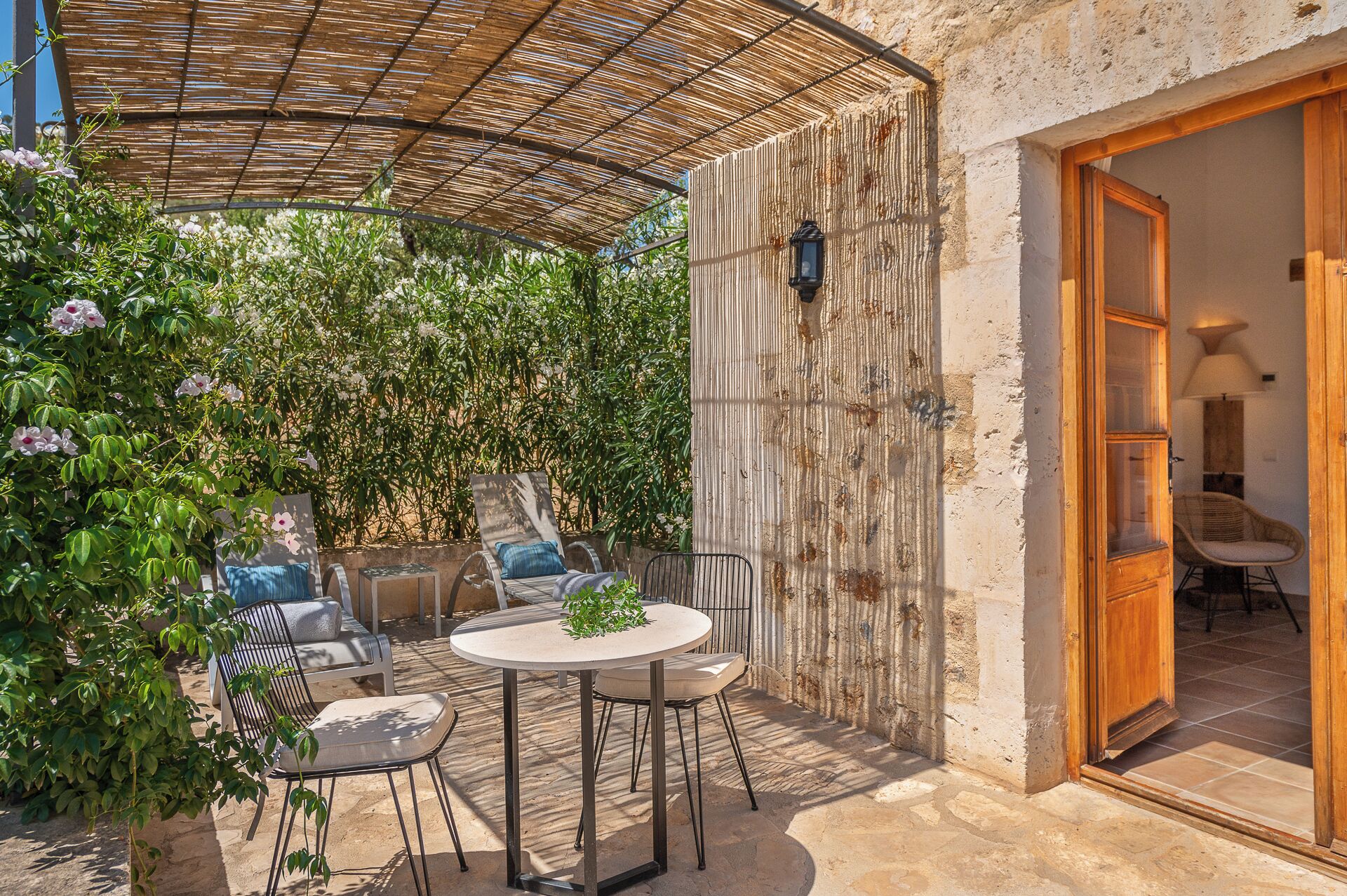 An outdoor patio with a round table and chairs, a wooden door, and a wall covered in climbing plants.