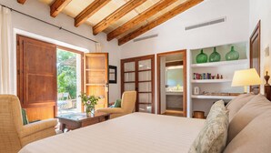 Une chambre à coucher avec un grand lit, des poutres en bois, une fenêtre, une porte, une étagère remplie de livres et une lampe.