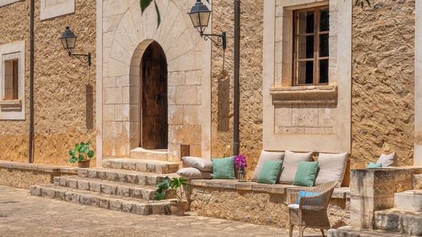 Un bâtiment en pierre avec une porte en bois, une fenêtre et un banc agrémenté de coussins.