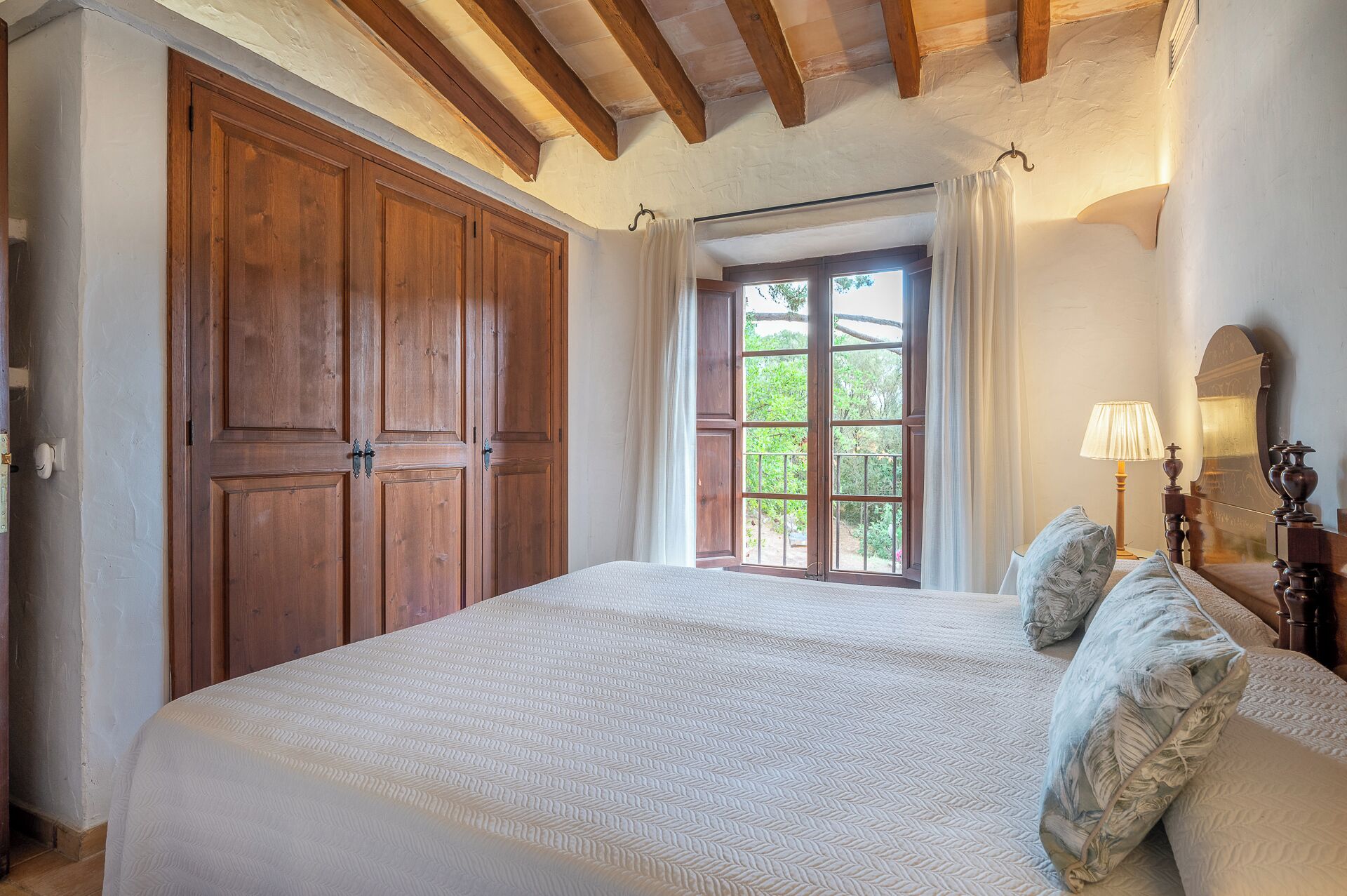 Une chambre à coucher avec un grand lit, une armoire en bois et une fenêtre avec des rideaux.