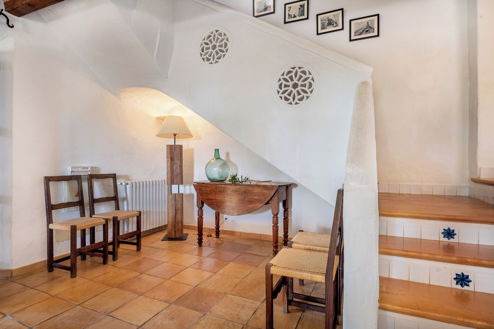 A staircase with a white wall, a wooden table with a lamp, and two chairs.