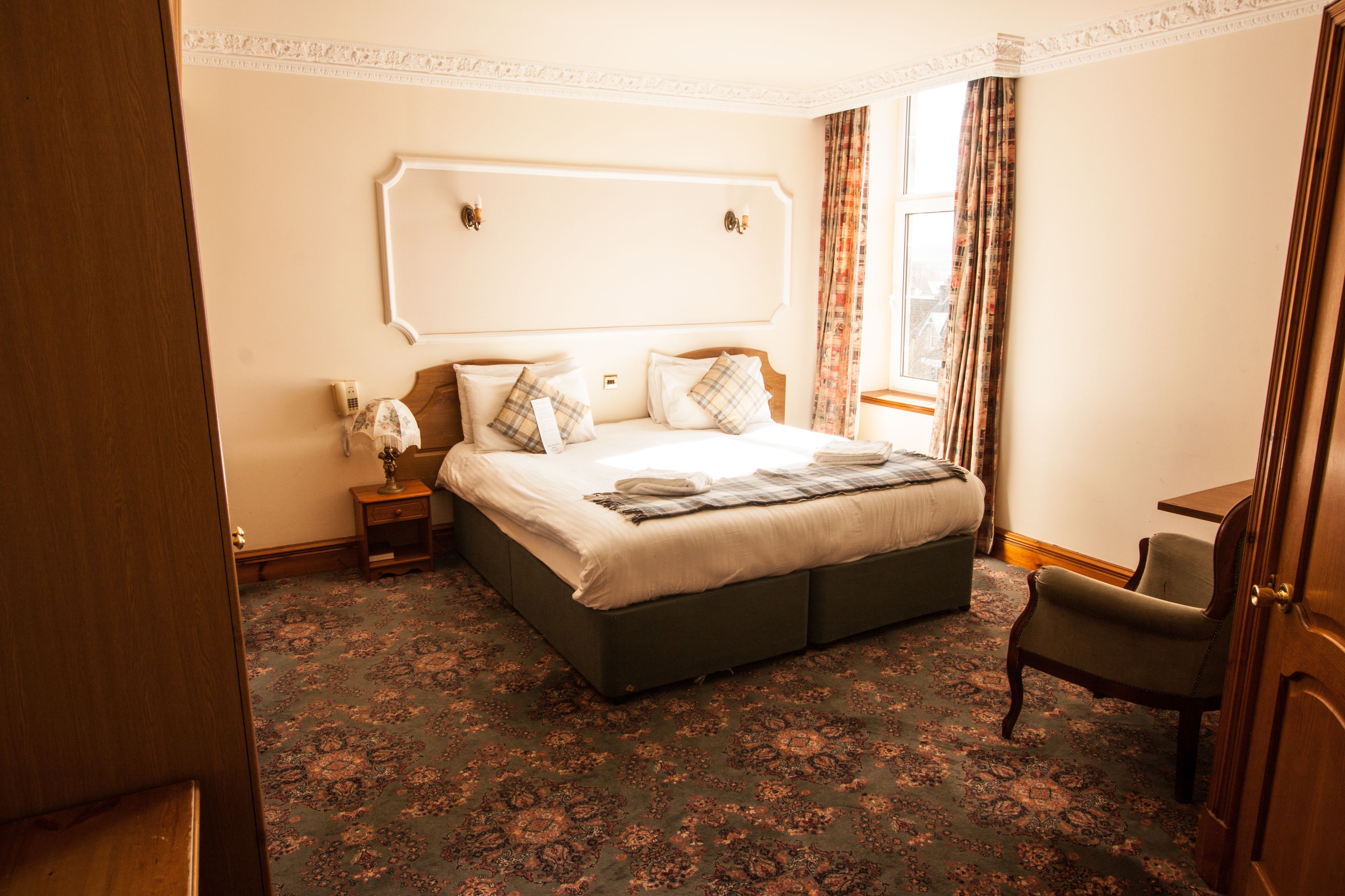 Habitación de hotel con una cama grande, una mesita de noche, una silla y una ventana con cortinas.