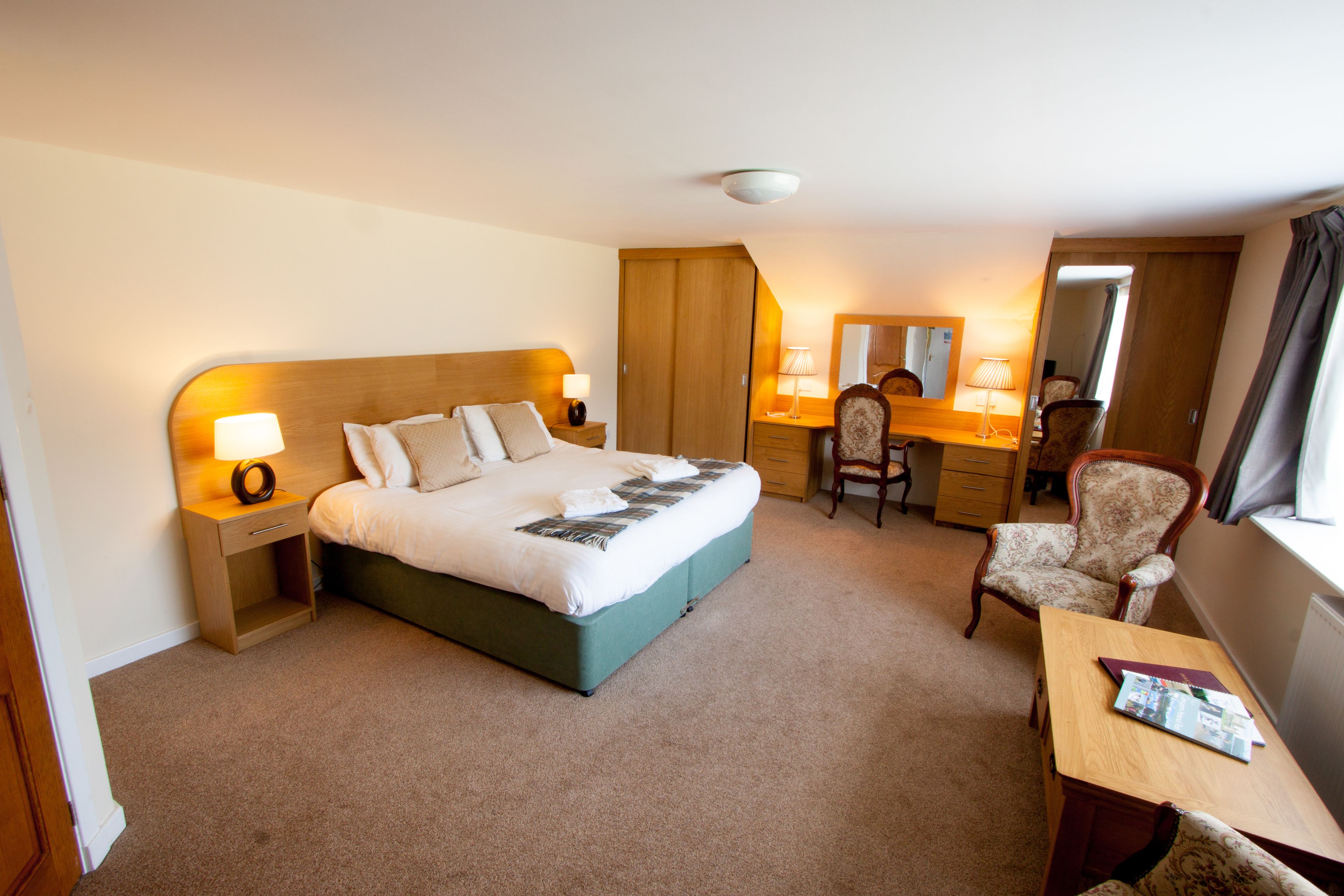 A hotel room with a bed, bedside tables, a desk, a chair, and a mirror.