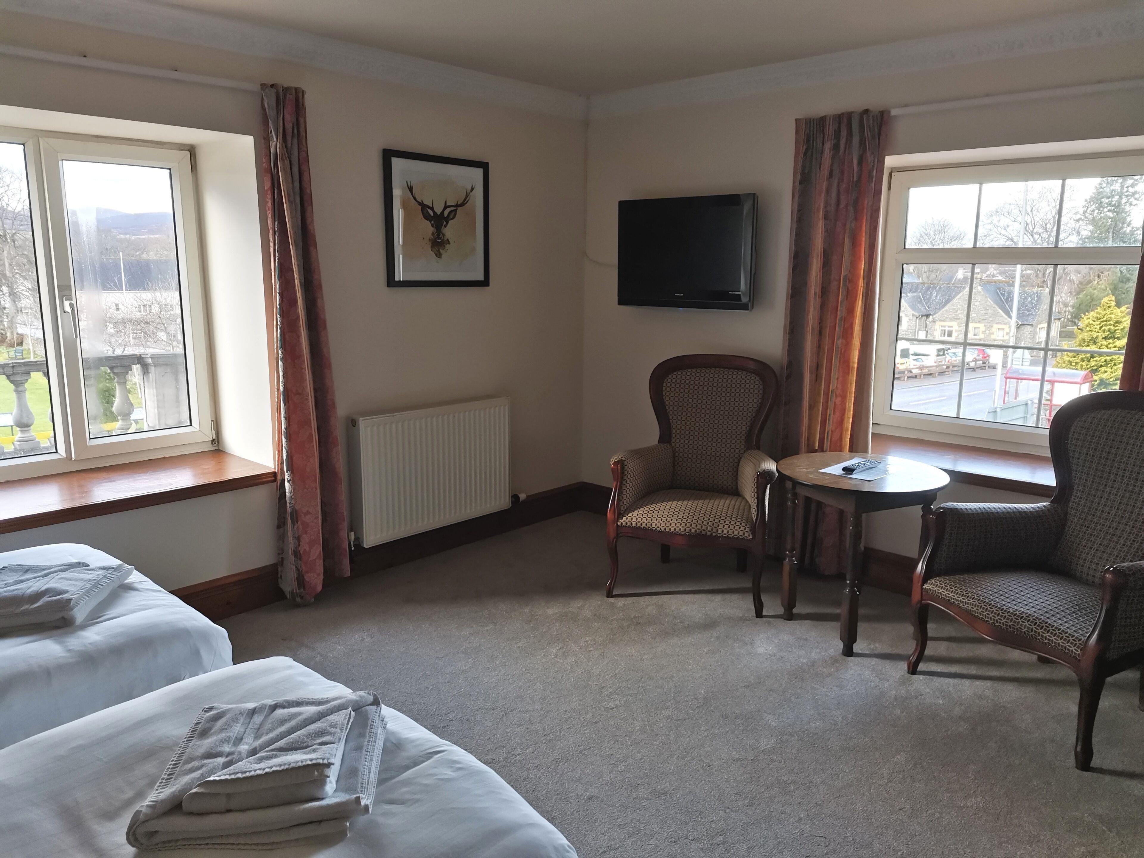 Habitación de hotel con dos camas, un radiador, un televisor y una ventana con vistas al exterior.