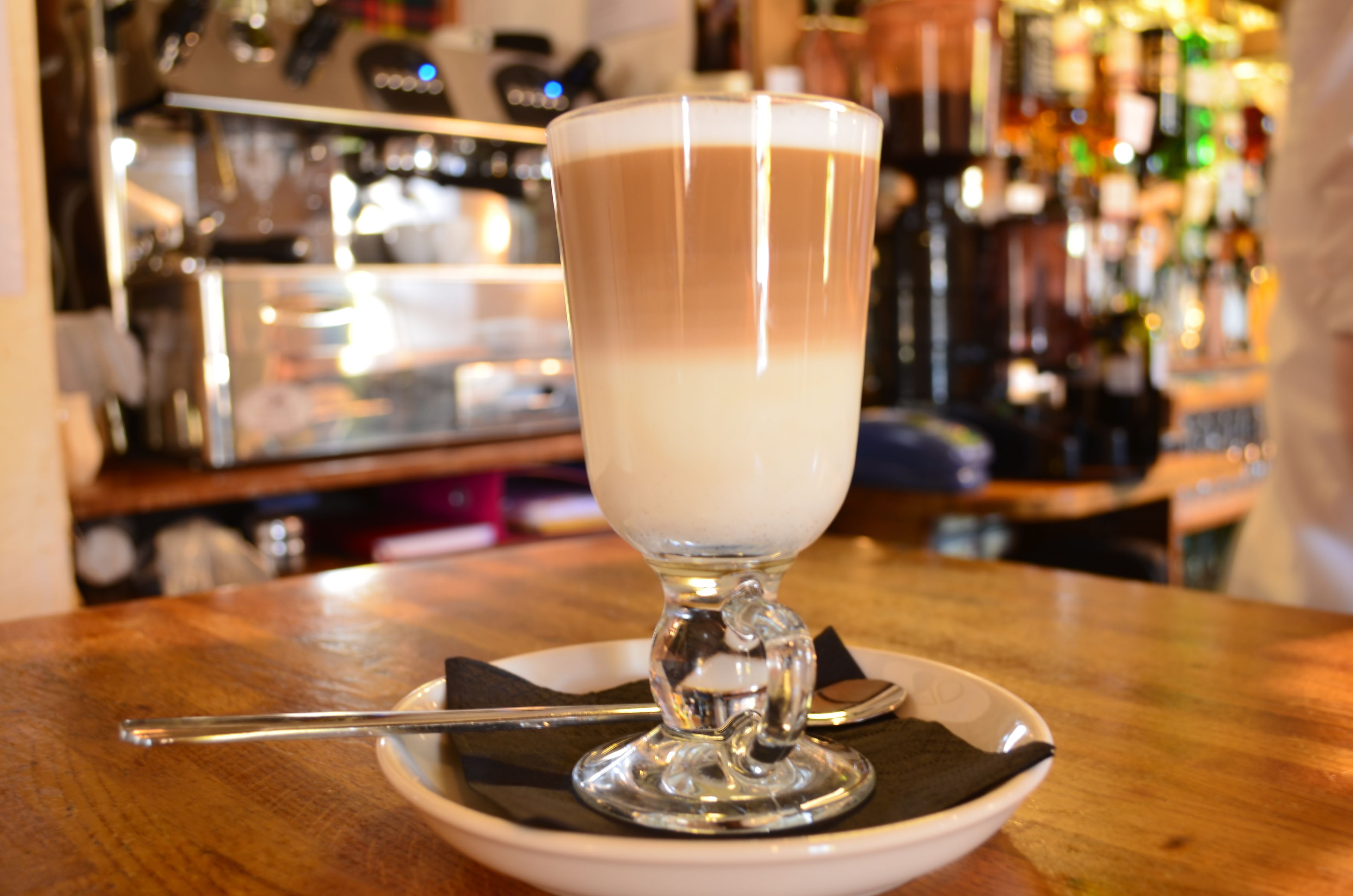 Un vaso de bebida en capas sobre un plato blanco con una cuchara, sobre una mesa de madera.