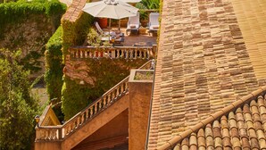 A building with a tiled roof, a balcony with outdoor furniture, and a view of the sea. - Petit Hotel Restaurante Ses Rotges - Adults Only (Capdepera)