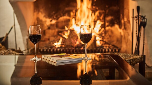 Two wine glasses on a table with a fireplace in the background. - Petit Hotel Restaurante Ses Rotges - Adults Only (Capdepera)