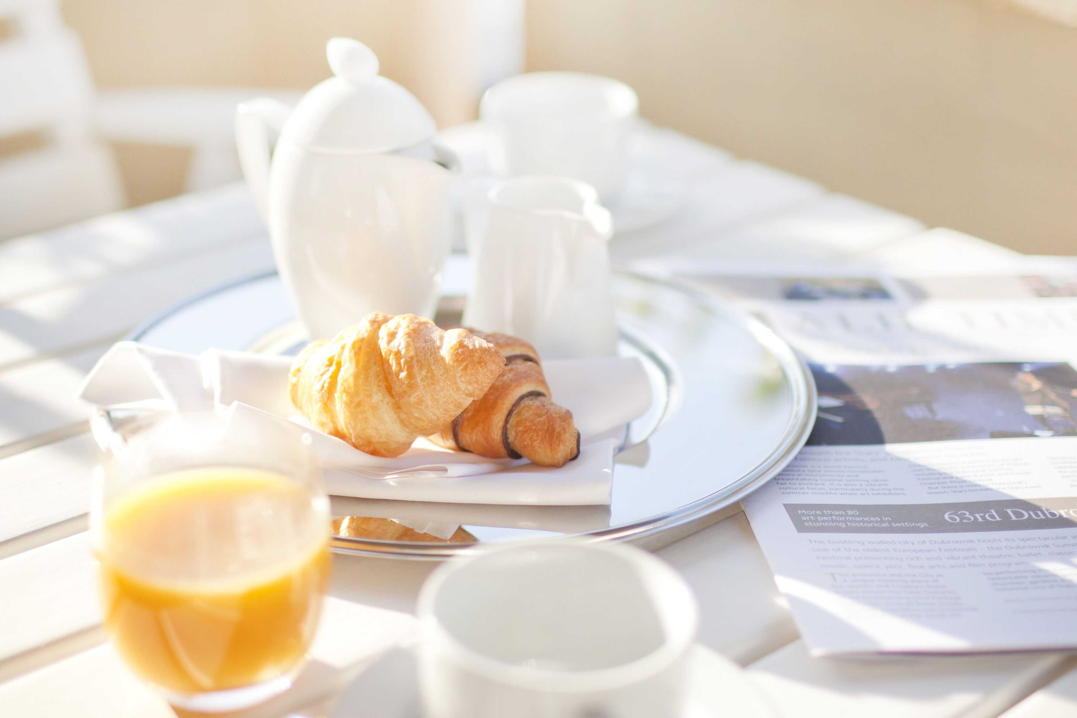 Un desayuno con cruasanes, tazas de café y un vaso de zumo de naranja sobre una mesa.