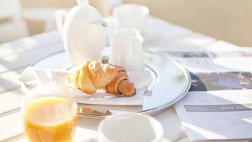 Un desayuno con cruasanes, tazas de café y un vaso de zumo de naranja sobre una mesa.