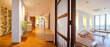 Een moderne hotel lobby met een houten vloer, een receptiebalie en een zithoek met ligbedden.