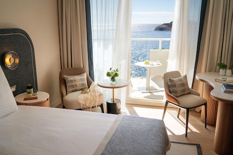 A hotel room with a bed, two chairs, a small table with a vase, and a view of the sea.. Hotel Croatia