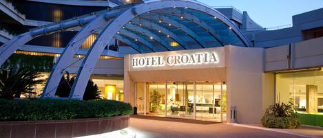 A modern hotel entrance with a glass facade and a curved metal structure above.