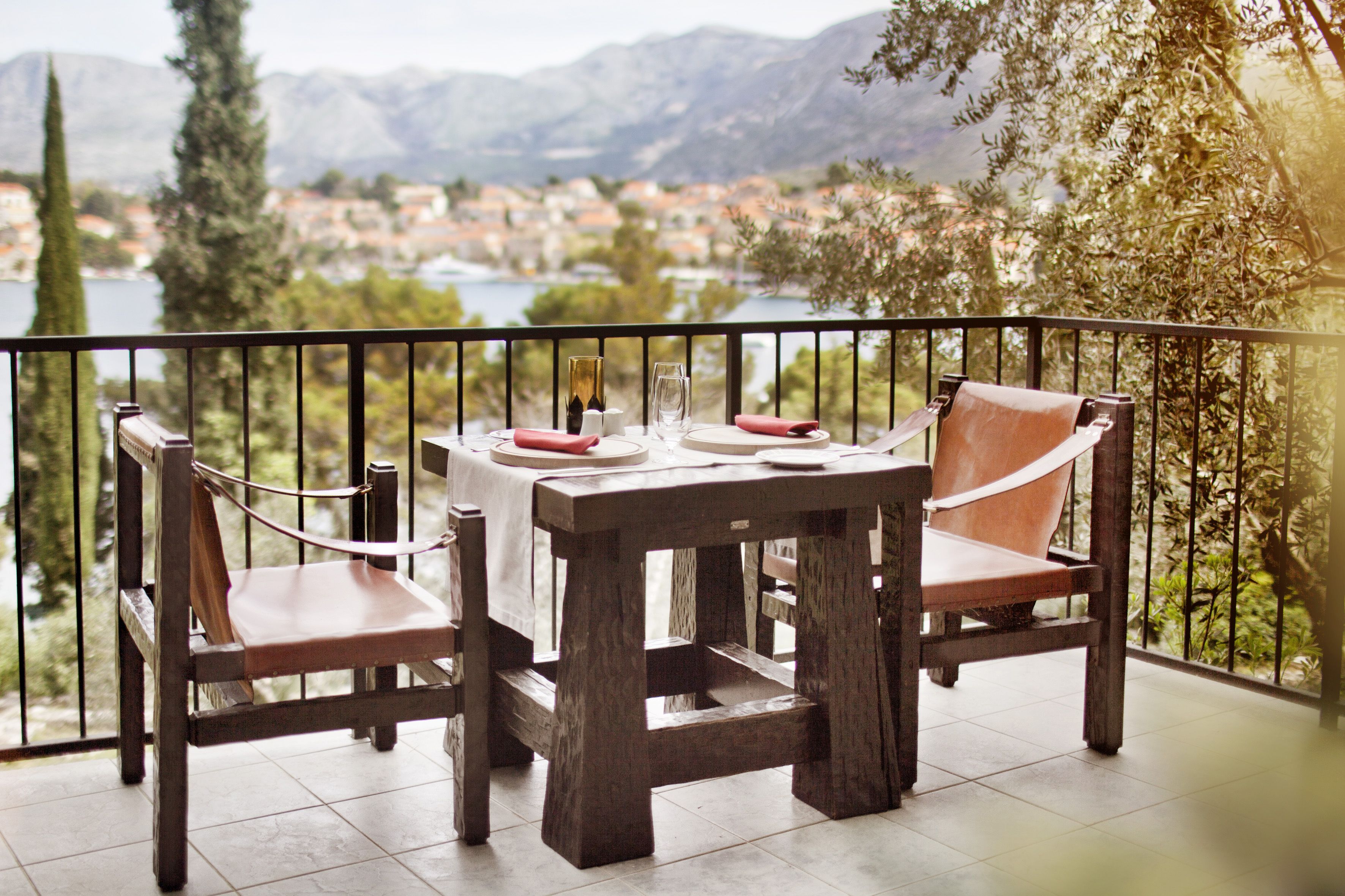 A wooden table with chairs on a balcony overlooking a lake and mountains.