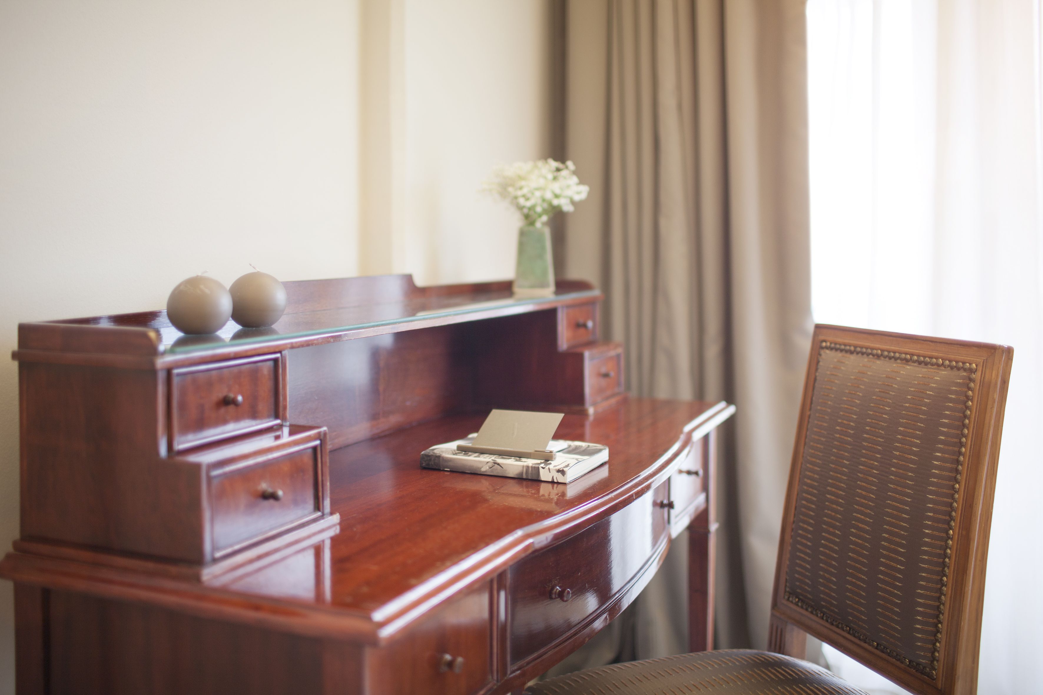 Un bureau en bois avec des tiroirs, un vase rempli de fleurs et un ordinateur portable.