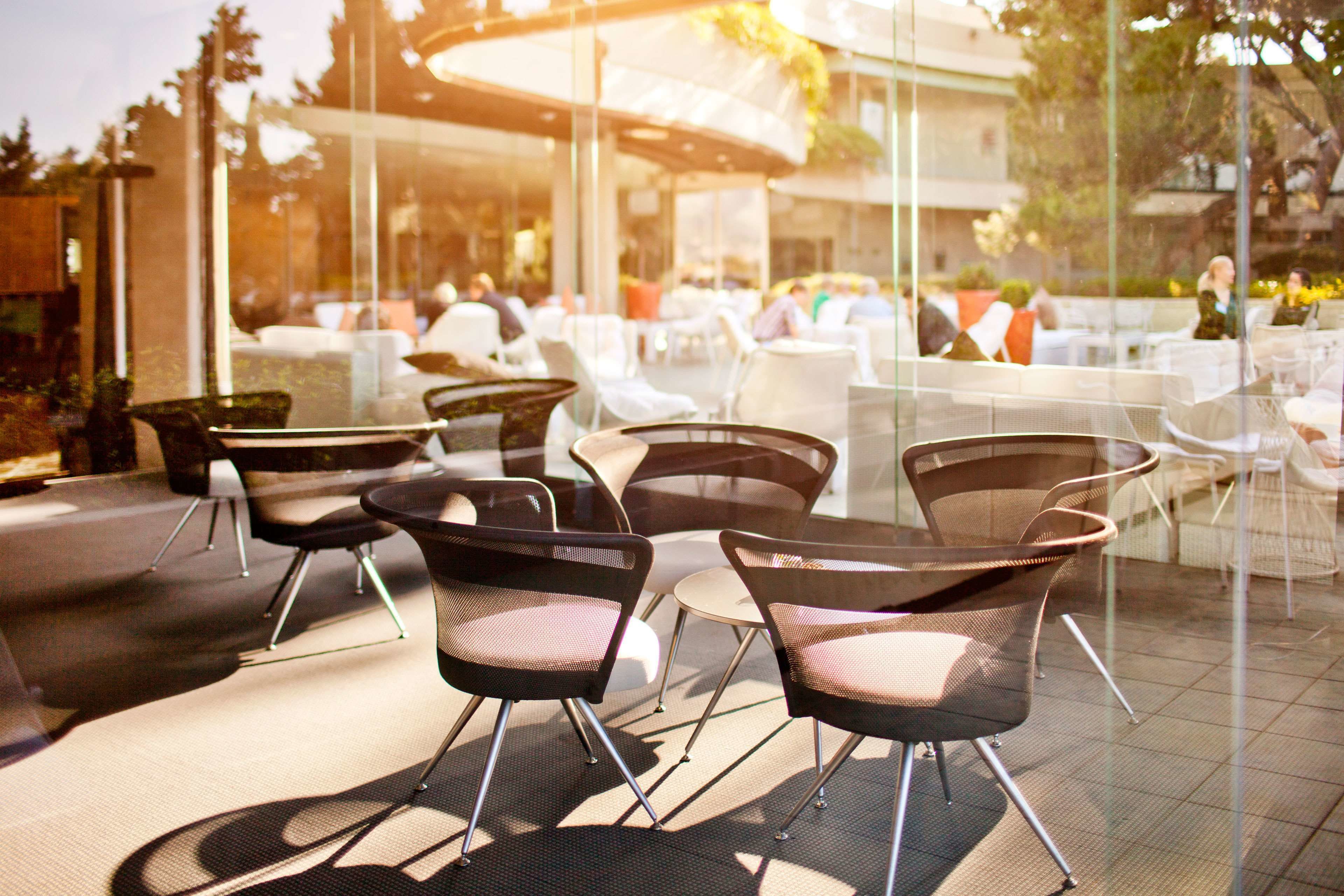 An outdoor seating area with modern chairs and tables, surrounded by glass walls and a view of a building in the background.