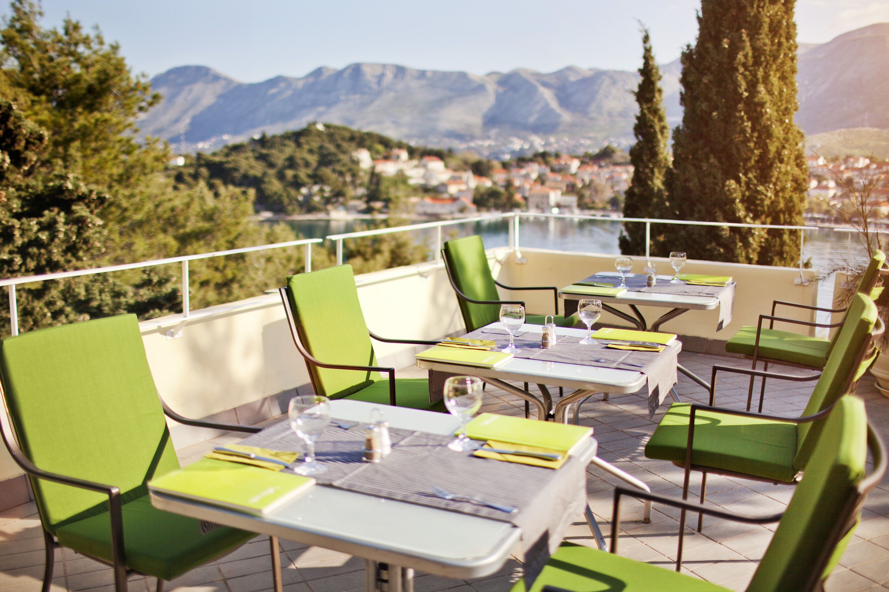 An outdoor dining area with tables and chairs, overlooking a scenic view of mountains and a town.